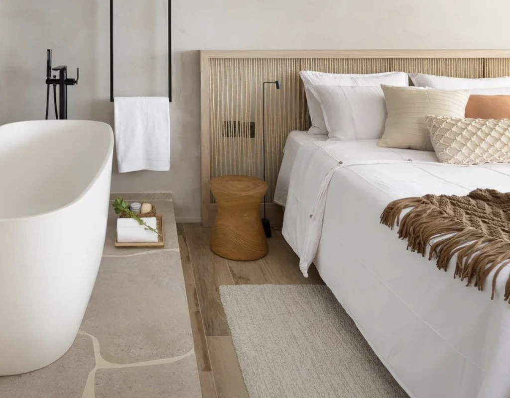 Banheira freestanding posicionada dentro do quarto de hotel de luxo, ao lado da cama, criando ambiente acolhedor e sofisticado.