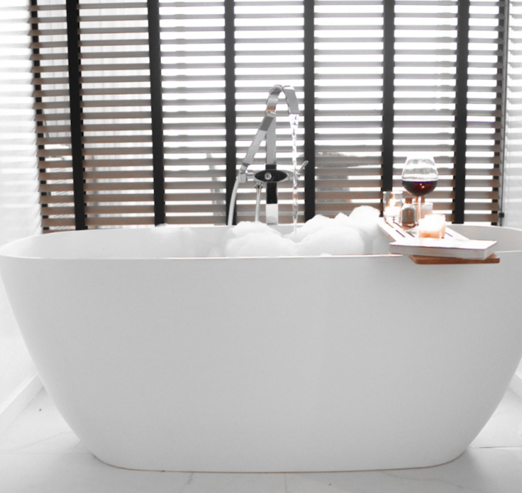 Banheira Bahia Sabbia com espuma, taça de vinho e iluminação suave em apartamento de luxo.